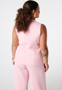 Roze mouwloze top met een gestructureerd ontwerp, gecombineerd met wijde broekspijpen. Gladde stof met een strakke silhouet; de achterkant toont de naaddetails.