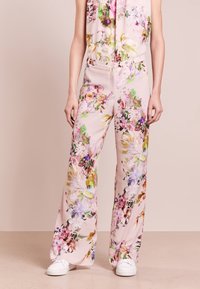 Bloemen jumpsuit met een lichtroze achtergrond; heeft levendige kleuren, brede benen en een getailleerde taille. Gecombineerd met witte sneakers.