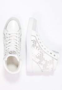 Zapatillas altas blancas con un diseño de malla perforada que presenta patrones florales, acentos de cuero suave y un logo redondo en la lengüeta.