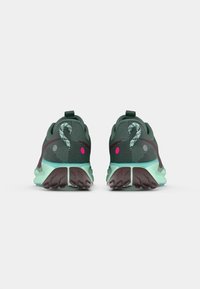 Un paio di scarpe da atletica verdi e aqua viste dal retro, con suole testurizzate e maniglie di sollevamento su uno sfondo semplice.