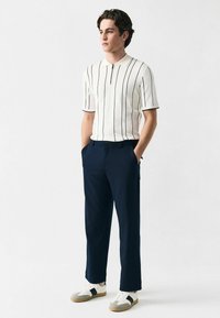 White short-sleeve polo shirt with navy vertical stripes, paired with navy trousers and white sneakers with gray accents.