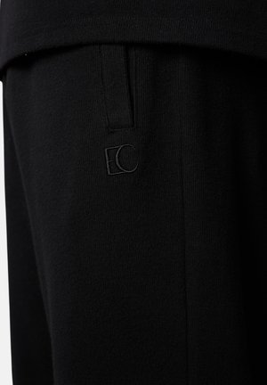 Schwarze Stoffhose mit einem dezenten "EC"-Logo in Stickerei nahe der Taschennaht, zeigt Strickstruktur und maßgeschneiderte Nähdetails.