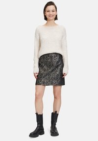 Weißer Strickpullover mit weitem Ausschnitt, kombiniert mit einem schwarzen, metallisch floral gemusterten Rock. Schwarze Leder-Ankle-Boots runden das Outfit ab.