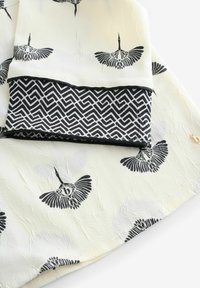 Schwarz-weiß gemusterter Stoff mit Krähen auf einem cremefarbenen Hintergrund. Hat am unteren Rand einen strukturierten schwarz-weißen geometrischen Rahmen.