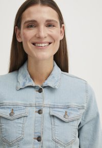 Plytelė šviesiai mėlynos džinsinės striukės su apykakle, dviem krūtinės kišenėmis ir ruda siūle. Puošia tamsios mygtukai ir šiek tiek išblukusi tekstūra.