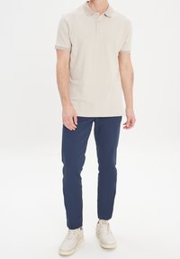 Beige polo triko s tříknoflíkovou légou a žebrovaným límečkem, spárováno s tmavě modrými kalhotami a světlými teniskami.