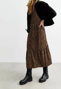 Maxi-mekko, jossa on leopardikuvio, esittelee kerroksellista muotoilua, yhdistettynä mustaan lyhythihaiseen takkiin ja mustiin nilkkureihin, luoden tekstuurisen mustavalkoisen ilmeen.