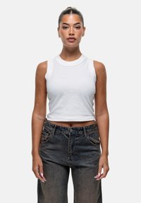 Biała, bezrękawnikowa crop top wykonana z bawełny, w połączeniu z ciemnoniebieskimi dżinsami z wysokim stanem, które mają kieszenie z przodu i zapięcie na guzik.