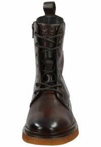 Botín de cuero marrón hasta el tobillo con puntera redonda, parte delantera con cordones y suela de goma texturizada. Presenta remaches decorativos y una lengüeta.