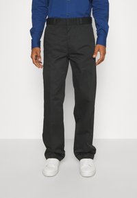 Svarta raka byxor med platt fram, tygmidja och sidofickor, kombinerat med vita sneakers och en blå skjorta med knappar.