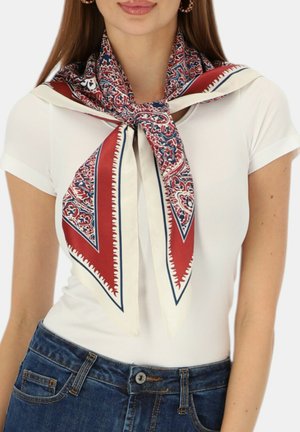 Kobieta w białej koszulce i niebieskich dżinsach z szalikiem w wzór czerwono-biało-niebieski zawiązanym na luźny węzeł wokół szyi.