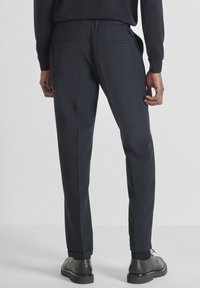 Marineblauwe broek met een getailleerde pasvorm, elastische tailleband, zijzakken, een gladde textuur en boorden bij de enkels, gecombineerd met zwarte schoenen.
