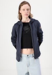 Marineblå zip-jakke med hette, lett stoff, frontlommer og en tettsittende design. Båret over en svart kort topp med rhinestones.