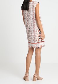 Robe sans manches présentant un motif floral en rouge, noir et blanc. Confectionnée en tissu léger, avec une coupe droite et un ourlet arrivant au genou.