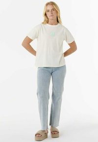T-shirt in cotone crema con scollatura tonda e grafica verde menta, abbinato a jeans dritti azzurri chiari e sandali beige senza lacci.