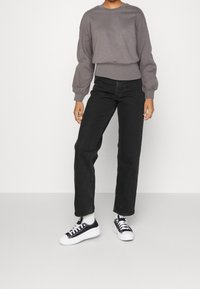 Felpa grigia a collo rotondo con una leggera texture, abbinata a jeans neri a vita alta e sneakers in tela nere con suole e lacci bianchi.
