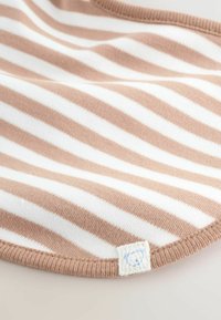 Tissu rayé brun clair et blanc avec des bords arrondis et une petite étiquette blanche arborant une silhouette d'ourson bleue.