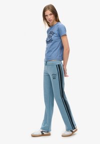 Niebieska bawełniana koszulka z czarnym nadrukiem graficznym, w zestawieniu z jasnoniebieskimi dresami z czarnymi paskami i detalami logo, uzupełniona o białe sneakersy.