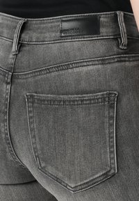 Gray denim jeans with a slightly distressed look, featuring a back pocket and a black leather label on the waistband.