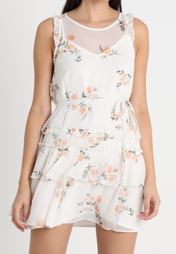 Weißes Blumenkleid mit Rüschendetails, das einen transparenten Ausschnitt und einen gestuften Rock hat. Das Blumenmuster enthält kleine orangefarbene und grüne Akzente.