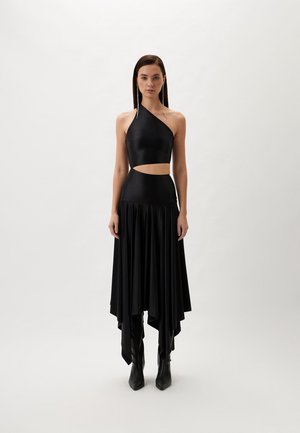 Black asymmetrical dress featuring a cutout at the waist, made of smooth fabric. The skirt is long with a flared design, paired with black boots.