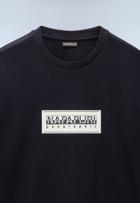 Sort bomulds t-shirt med rund hals og en rektangulær hvid grafisk detalje med "NAPAPIJRI" og "geographic" i fed sort tekst.