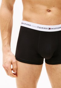 Melni kokvilnas bokseršorti ar baltu elastīgu jostasvītru, kas rotāta ar zīmolu "TOMMY HILFIGER" un maziem logo akcentiem.