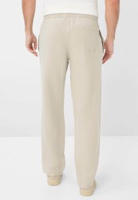 Light beige, loose-fitting pants with an elastic waistband and back pocket. Fabric appears textured with a soft, breathable quality.
