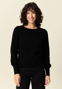 Musta neulepaita pitkillä hihoilla, pyöreällä kaula-aukolla ja ribbaatuilla hihansuilla. Pehmeä kangas ja sukkulamainen muotoilu ilman kuvioita tai lisäkorostuksia.