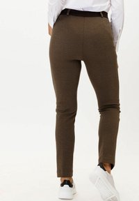 Bruna texturerade byxor med slim fit och svart midjeband, kombinerat med vita sneakers, avbildat bakifrån.