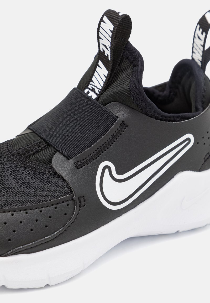 Zapatilla deportiva negra con parte superior texturizada, cierre tipo correa, prominente logo de Nike en blanco y suela blanca. Presenta perforaciones para mayor transpirabilidad.