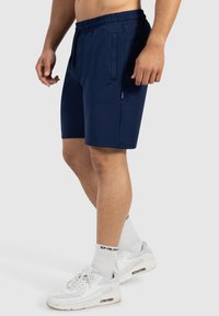 Marineblauwe sportbroekjes met een elastische tailleband, zijzakken en een gladde textuur. Draagt met witte sneakers en sokken.
