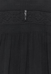 Robe noire avec un panneau en dentelle transparente, présentant des coutures horizontales et une texture plissée. Le tissu est léger et fluide.