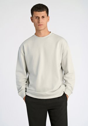 Hellgrauer Sweatshirt mit Rundhalsausschnitt, langen Ärmeln und lockerer Passform, kombiniert mit schwarzen Hosen. Glatte Stofftextur, schlichtes Design.