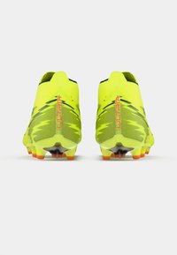 Jaskrawożółte korki piłkarskie z siateczkową cholewką i czarnymi akcentami, charakteryzujące się smukłym designem i wielokolorowymi kołkami zapewniającymi przyczepność.