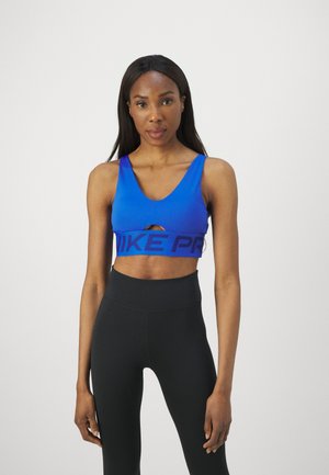 Mėlynas sportinis liemenukas su apvaliu iškirpimu, išpjovimu ir plačia juoda juosta su "NIKE PRO" logotipu. Suderintas su aukšto juosmens juodomis leggings.