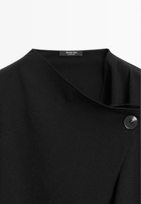 Cappotto in lana nera con colletto a scialle, caratterizzato da un solo bottone nero e una texture liscia. L'etichetta reca la dicitura "Massimo Dutti", indicando il marchio.