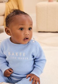 Světlomodrý pletený komplet s bílými akcenty a nápisem „BAKER“. Má žebrovanou texturu a knoflíkový detail na rameni.