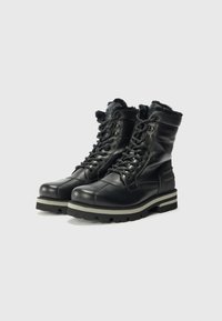 Botas de cuero negro con tobillo alto, que cuentan con un forro de felpa, cordones resistentes y una suela gruesa y robusta diseñada para la durabilidad.