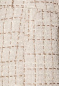 Strukturalna tkanina w kremowym i beżowym kolorze z wzorem w kratkę. Miękki, tkany materiał o delikatnym połysku i widocznych nitkach w całej powierzchni.