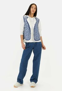 Blue floral-patterned vest with a white lining, worn over a white hoodie, paired with loose blue denim pants and light sneakers.