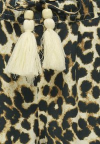 Látka s leopardím potiskem v kombinaci černé, hnědé a krémové barvy; bílé třásně s dřevěnými korálky dotvářejí pás.