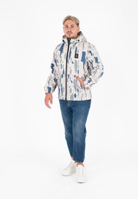 Lichtgewicht, gevoerde jas met capuchon in een abstract patroon van wit, blauw en grijs, met rits aan de voorkant en elastische manchetten, gecombineerd met denim en witte sneakers.