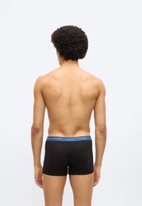 Μαύρα βαμβακερά ανδρικά μποξεράκια με μπλε ζώνη μέσης που φέρει το λογότυπο "TOMMY HILFIGER". Φαίνονται από πίσω, παρουσιάζοντας την εφαρμογή και το σχέδιο.