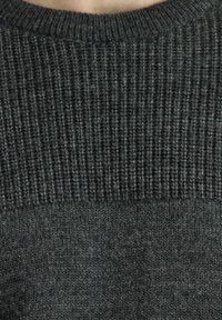 Suéter gris oscuro con textura acanalada en la parte superior y un tejido de punto más suave en la parte inferior. Cuello redondo clásico.