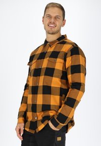 Langærmet plaid skjorte med sorte og orange tern, to brystlommer og knaplukning. Fremstillet af et tekstureret stof.