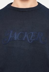 Pulover tricotat navy cu un logo texturat „JACKER” într-o nuanță mai închisă, design clasic cu gât rotund și textură de țesătură netedă.