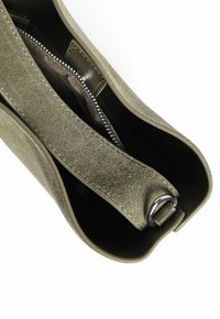 Sac en daim vert olive avec une texture lisse, poche intérieure zippée et accents en métal. Large bandoulière pour le porter.