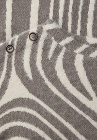 Tissu à motif zébré dans des tons doux beige et marron. Présente deux boutons marron sur le côté gauche, surface texturée avec une finition duveteuse.