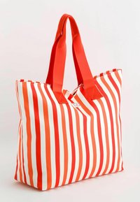 Červenobílá pruhovaná taška přes rameno s tlustými červenými uchy a obdélníkovým tvarem. Vyrobena z odolného textilu s kontrastním šitím.